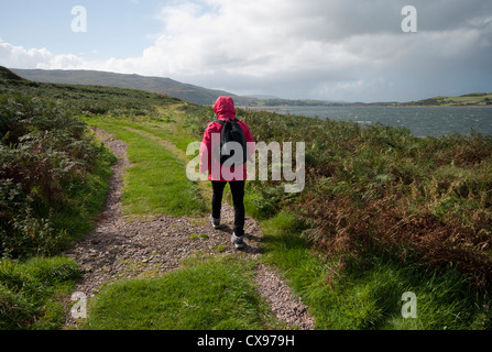 Vista posteriore di una donna persona passeggiate attraverso la campagna di indossare indumenti impermeabili e uno zaino Foto Stock