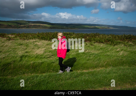 Vista laterale di una donna persona passeggiate attraverso la campagna di indossare indumenti impermeabili e uno zaino Foto Stock