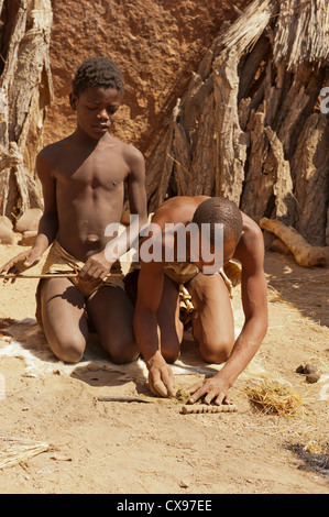 Due giovani ragazzi illuminazione di un fuoco usando strumenti tradizionali in Damaraland, Namibia Foto Stock