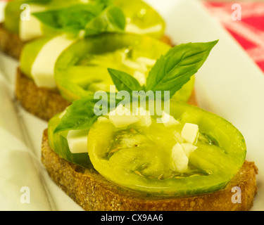 Fresh bruschetta con cimelio di verde formaggio pomodori e basilico su piastra bianca Foto Stock