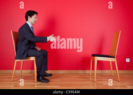 Accordo di stretta di mano tra un imprenditore e una sedia accanto ad una parete rossa Foto Stock