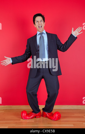 Happy businessman accanto a una parete rossa con scarpe clown Foto Stock