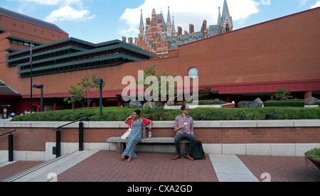 Un uomo e una donna seduta su una panchina al di fuori della British Library con San Pancrazio hotel in background Londra Inghilterra REGNO UNITO Foto Stock
