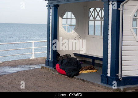 Donna senzatetto (nascosto che giace sotto il sacco a pelo) dormire in rifugio sul lungomare vicino alla spiaggia e mare Aberystwyth Wales UK Foto Stock