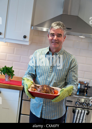 Sorridendo rilassato uomo fiducioso nella cucina contemporanea tenendo un caldo cucinato al momento pasto di pollo arrosto e verdure Foto Stock