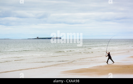 Un pescatore di fusione il suo stelo fuori per vedere dalla spiaggia Bamburgh in Northumberland. Foto Stock
