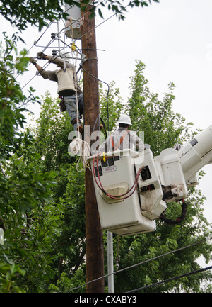 Un uomo dentro a sollevare la benna aiuta un altro uomo su un polo di alimentazione installare nuove linee elettriche nella città di Oklahoma, Oklahoma. Stati Uniti d'America. Foto Stock