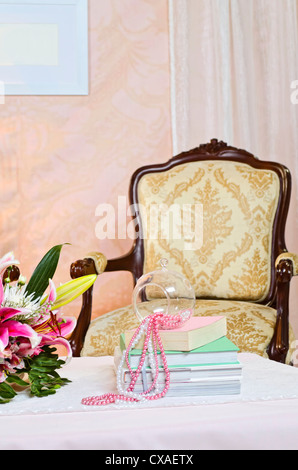 Configurazione Studio di sedia e tavolo da caffè con libri, perle, e fiori sulla parte superiore Foto Stock
