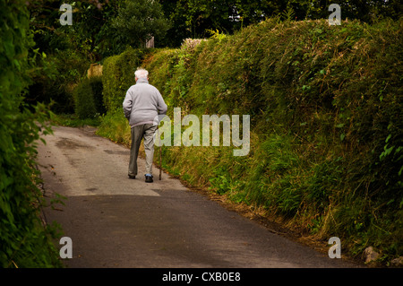 Uomo anziano con bastone passeggiate lungo una corsia rurale Foto Stock