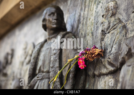 Primo piano di fiori posti sul braccio della statua di Cristoforo Colombo presso il Monumento a Colombo a Barcellona, Spagna Foto Stock