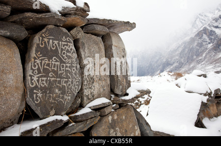 Vecchio Mani pietre inscritte con un mantra buddista e coperti di neve, Langtang Valley, Nepal Foto Stock