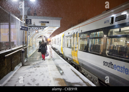 Piattaforma innevata, donna in pantaloni rossi e treno sud-orientale alla stazione di Lewisham Foto Stock