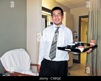 Sorridente giovane uomo asiatico in camicia & Striped tie offre la cena in stile al paziente in ospedale svedese Edmonds Washington Foto Stock