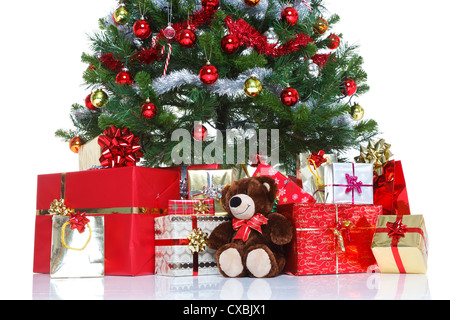 Albero di Natale decorato con baubles tinsel e circondato da regalo presenta e un orso di peluche Foto Stock