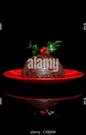 Foto di un tradizionale budino di Natale con agrifoglio e bacche sulla parte superiore, su uno sfondo nero. Foto Stock