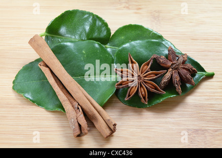 Anice stellato (Illicium verum - entrambi i lati del contenitore mostrato), cannella e kaffir lime (Citrus hystrix) foglie su un tagliere, Foto Stock