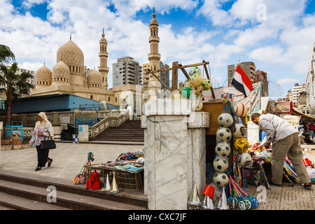 El-Mursi Abul Abbas moschea con uomo vendita di giocattoli in strada in primo piano. Alessandria, Egitto Foto Stock