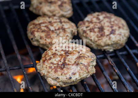 Agnello gli hamburger sul grill. Quattro hamburger di agnello essendo alla griglia su orange fiamme. Foto Stock