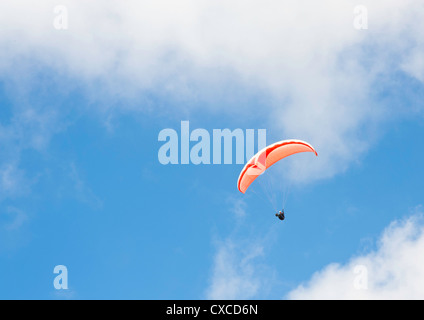 Parapendio singolo con un rosso e bianco con il paracadute in volo sotto un cielo blu e nuvole Foto Stock