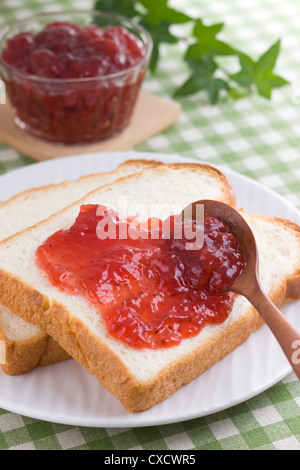 Diffusione di confettura di fragole su pane Foto Stock