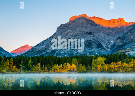 La luce del mattino gli schizzi le punte del monte Kidd e il vicino paese di Kananaskis picchi mentre riflette sulla superficie di stagno a cuneo. Foto Stock