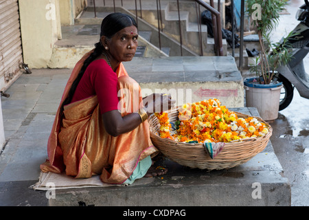 Donna indiana la vendita di calendula fiori in un cestello per la puja indù offerte. Puttaparthi, Andhra Pradesh, India Foto Stock