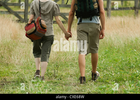Giovane camminando nel campo tenendo le mani, vista posteriore Foto Stock