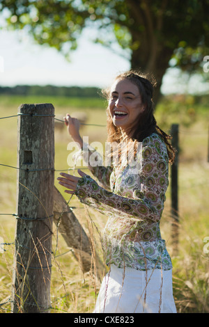 Giovane donna in piedi da recinzione in campo Foto Stock