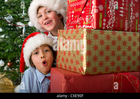 Boys peeking intorno a pila di regali di Natale Foto Stock