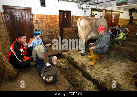 Tirolo, padre e figli vedere un coltivatore che munge nel fienile Foto Stock