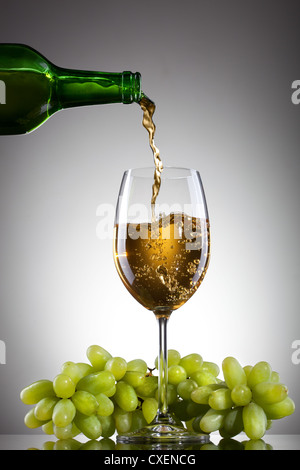 Vino bianco versando in vetro dalla bottiglia con uva verde Foto Stock