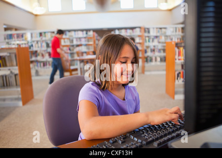 Ragazza utilizzando computer in biblioteca Foto Stock