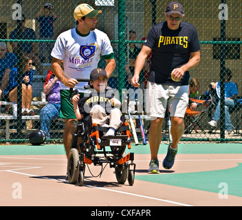 Player e pullman su un softball team nel miracolo League facendo una corsa per la prima base dopo un colpo. Foto Stock