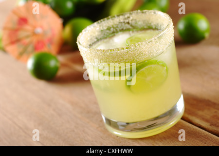Limonata Fresca di verde lime in zucchero-bordati di vetro su tavola di legno con tigli e una carta arancione ombrellone in retro Foto Stock