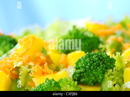 Insalata fresca fatta di broccoli, mango, la carota e la lattuga di fronte a uno sfondo blu (messa a fuoco selettiva, messa a fuoco sulla parte anteriore) Foto Stock