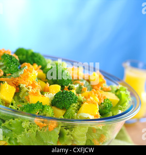 Broccoli-mango--carota insalata di lattuga in una ciotola di vetro con succo di arancia medicazione in background Foto Stock