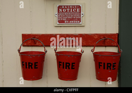 Tre fire secchielli riempiti con sabbia appendere in una linea pronto per l'uso in caso di incendio. Foto Stock