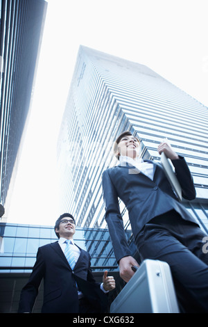 Una donna e un uomo d affari con valigette in esecuzione tra edifici per uffici Foto Stock