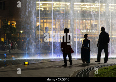 3 persone (contorni) a piedi nella parte anteriore di una moderna fontana della Petronas Tower park di Kuala Lumpur in Malesia Foto Stock