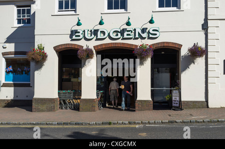 Un uomo esce da un locale negozio budgens come altro entra Foto Stock