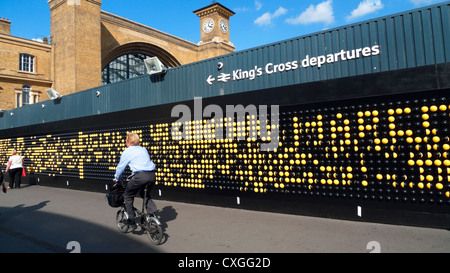 L'uomo del pendolari passa davanti all'installazione artistica interattiva del Song Board alla stazione ferroviaria di King's Cross su una bici Brompton a Londra, Regno Unito KATHY DEWITT Foto Stock