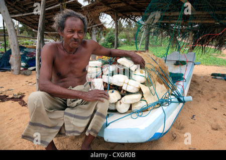 Pescatore locale seduto su una barca con la sua pesca reti impilate sulla parte superiore, Waikkal, Sri Lanka Foto Stock