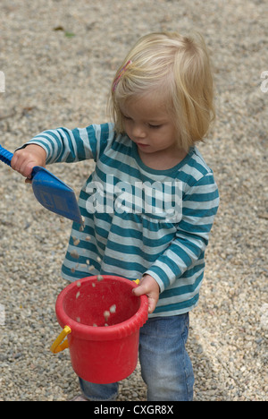 Bambino biondo toddler girl 1 anno di età giocando con i ciottoli, secchi e pale in estate park Foto Stock