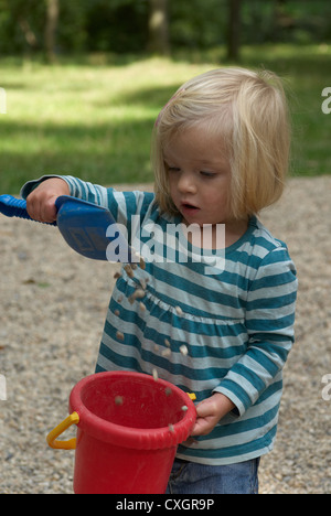Bambino biondo toddler girl 1 anno di età giocando con i ciottoli, secchi e pale in estate park Foto Stock