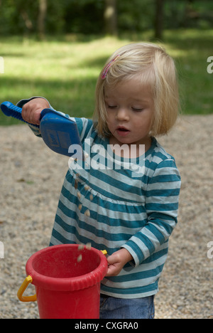 Bambino biondo toddler girl 1 anno di età giocando con i ciottoli, secchi e pale in estate park Foto Stock