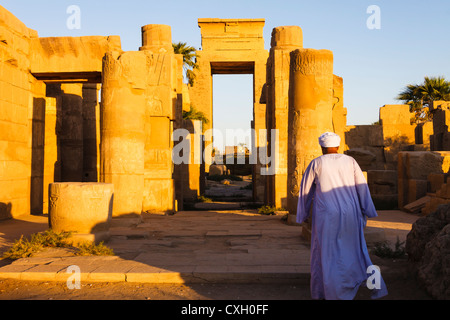 Guardia in Jellabiya passeggiate al tramonto verso una porta monumentale nel tempio Karkak, Luxor, Egitto Foto Stock