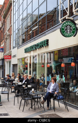 La gente seduta sui posti a sedere fuori a Starbucks Coffee shop nel centro della città di Arthur Square, Belfast, County Antrim, Irlanda del Nord, Regno Unito Foto Stock