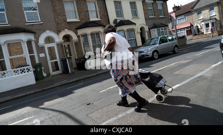 Nero donna che attraversa la strada con un carrello della spesa di Walthamstow Londra Inghilterra REGNO UNITO Foto Stock