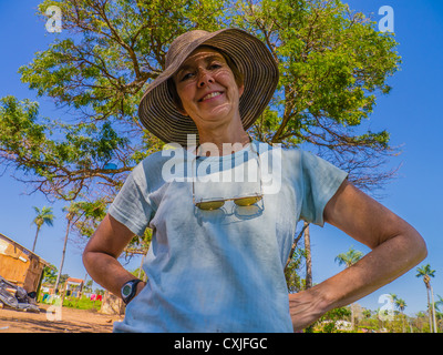 Un Habitat for Humanity Paraguay volontario, di mezza età donna caucasica sorride al di fuori in piedi sotto un albero e il profondo blu del cielo. Foto Stock