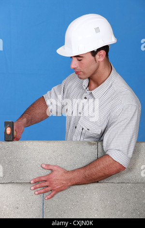 Muratore toccando giù un blocco di muro Foto Stock